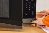 A thumb pressing a button on the Magic Chef 1.1 Microwave
