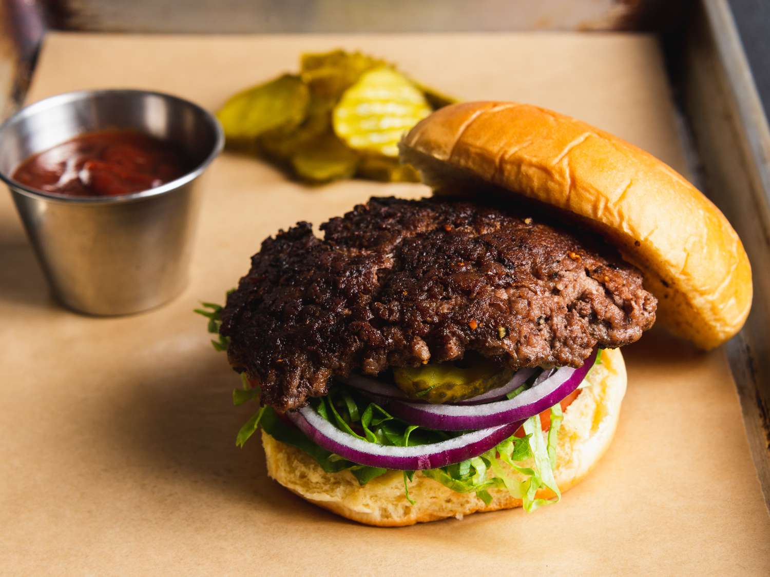 A smashed burger on a bun with pickles, red onion, lettuce, and tomato, with the top bun slightly off.