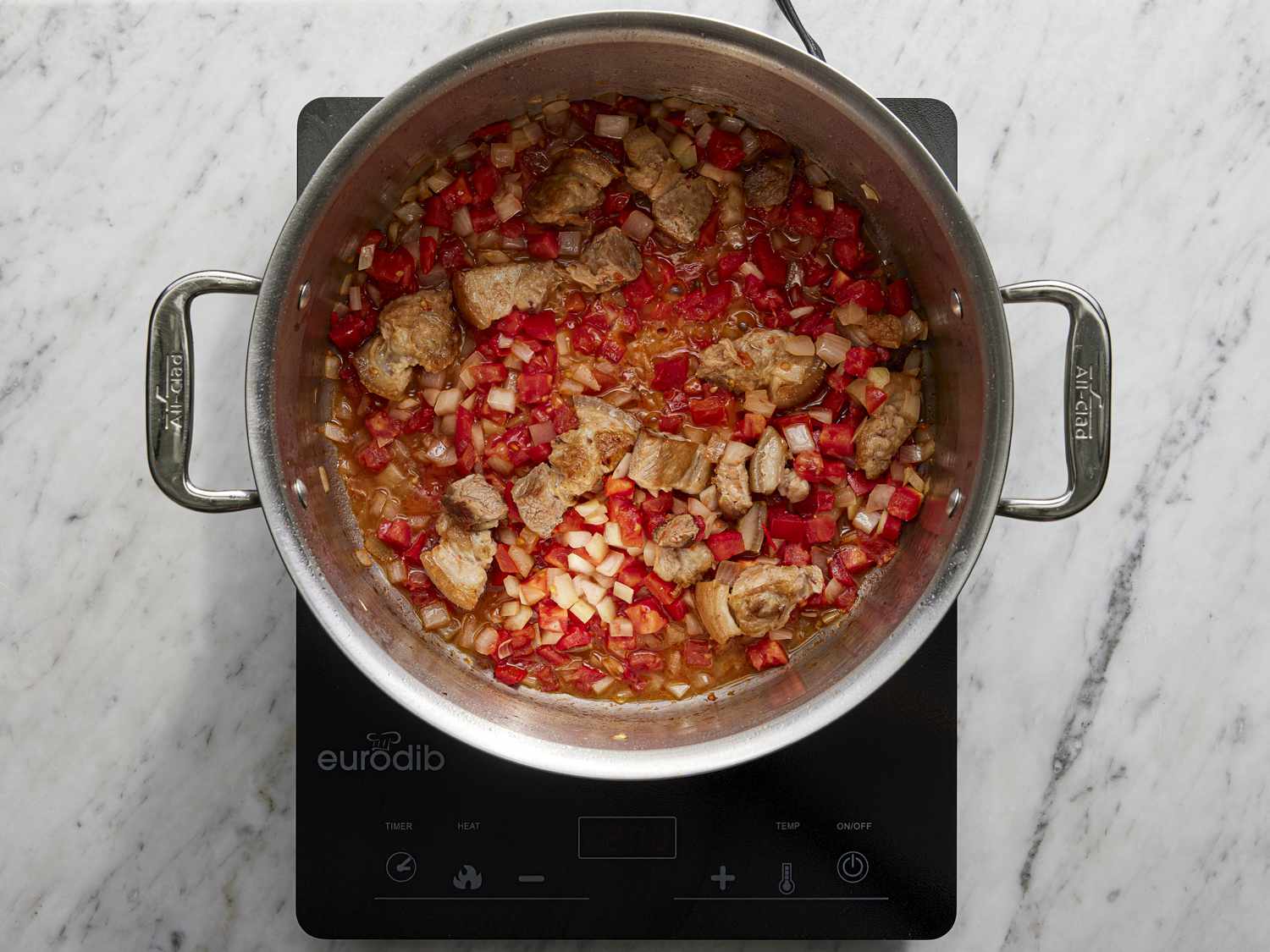 Overhead view of tomato and meat in a pot cooking.