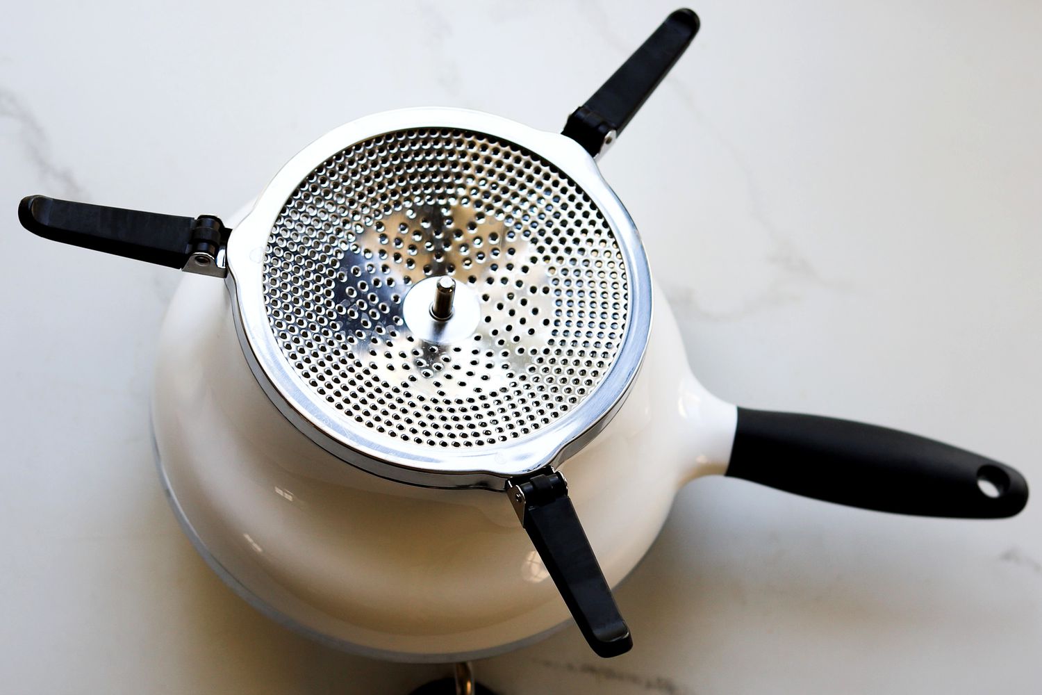 The OXO food mill flipped over on a marble surface so you can see the perforations on the bottom