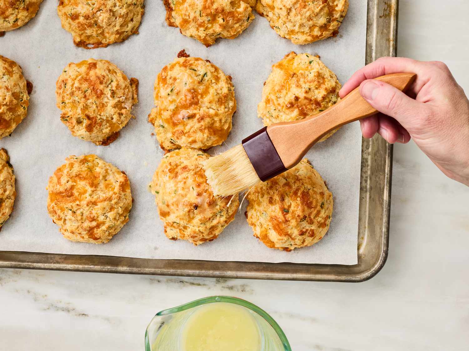 Brushing butter over baked drop biscuits on a tray