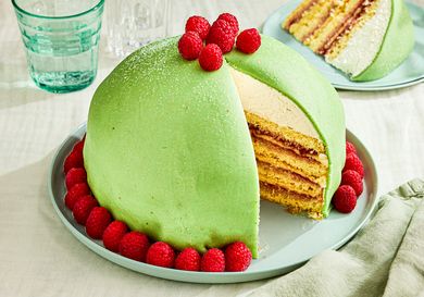 A sliced Princess cake garnished with raspberries on a plate showing its layered interior filling and marzipan cover