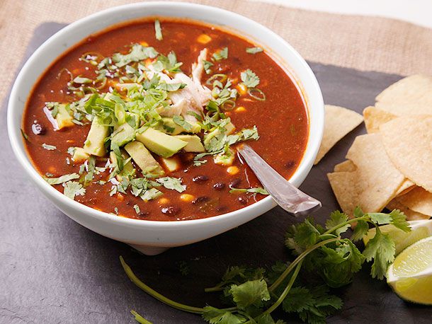 A bowl of tortilla soup with lots of herbs and avocado as garnish.