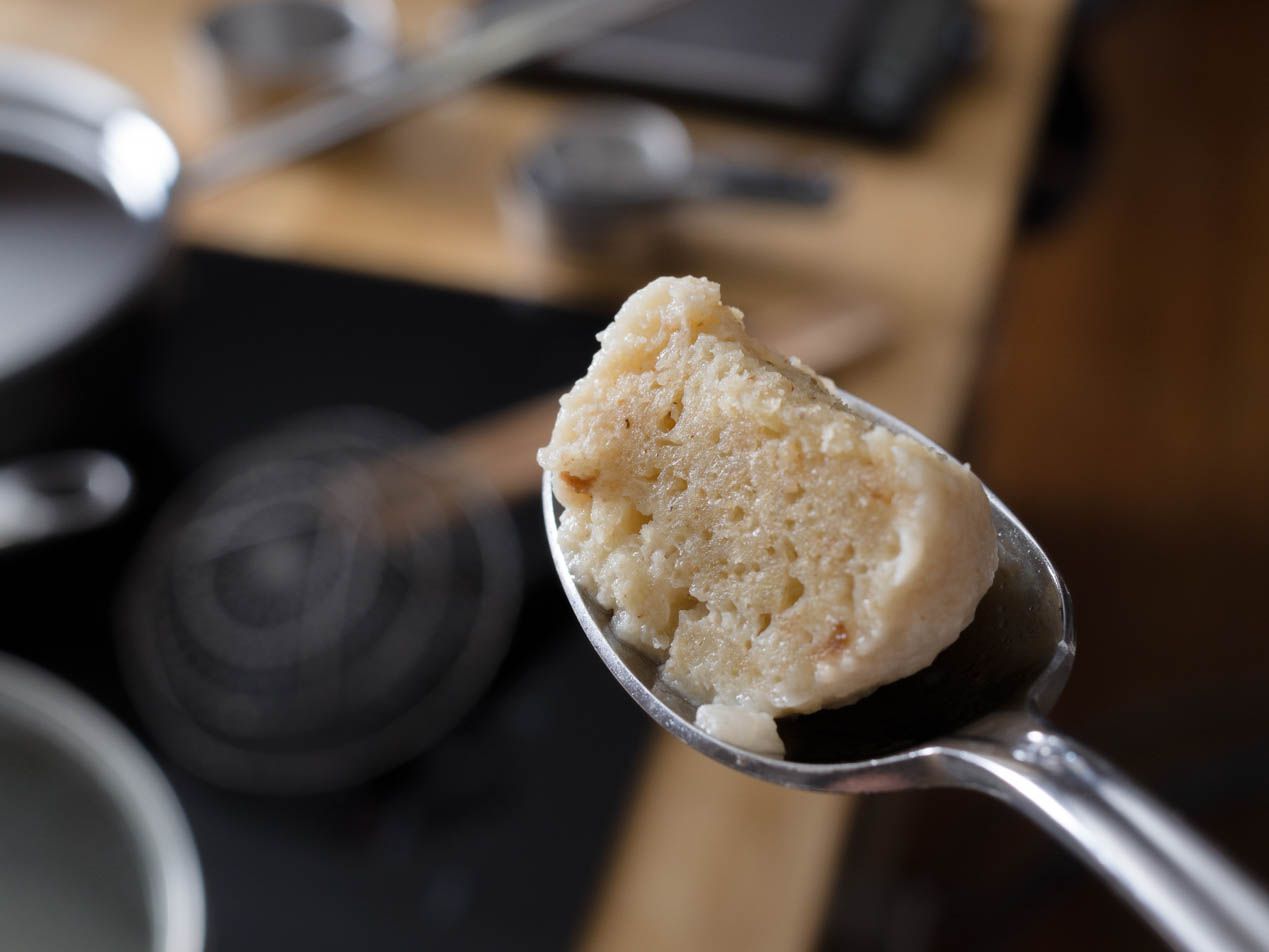 Close-up of a spoon holding a wedge of cooked matzo ball. The internal structure of the ball is in sharp focus.