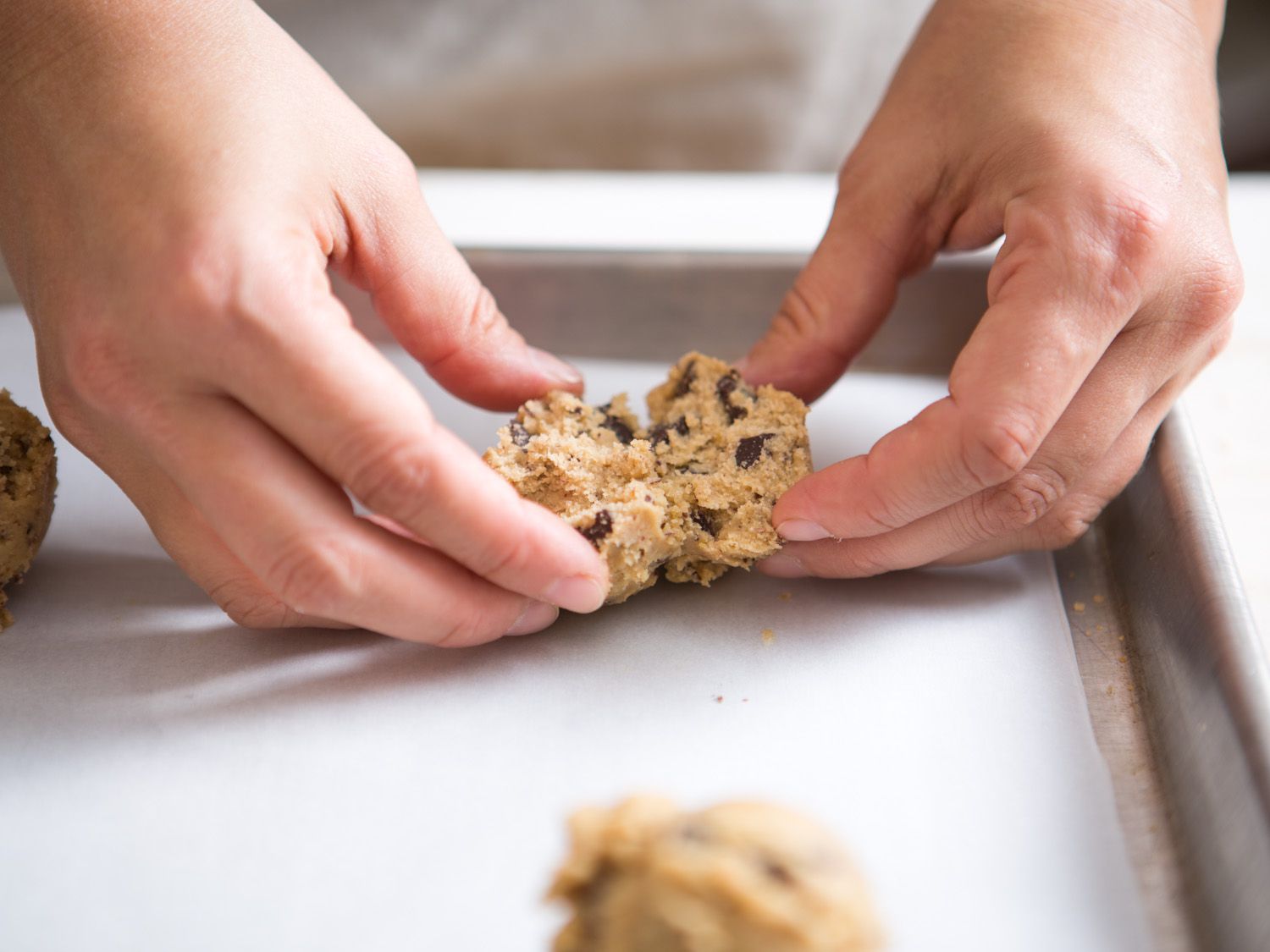 Hands splitting a ball of chocolate chip cookie dough in half 
