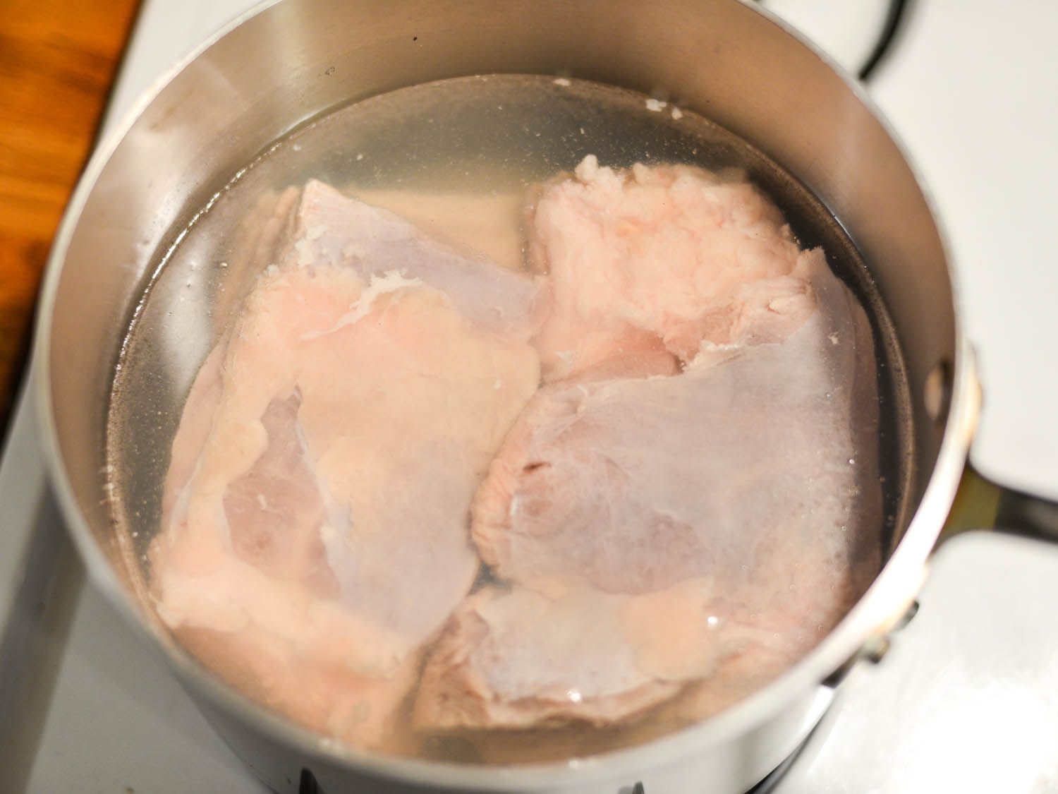 Two cuts of pork belly being brought to a boil in salt water.