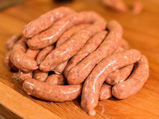 Uncooked links of merguez sausage sitting on a wooden cutting board.