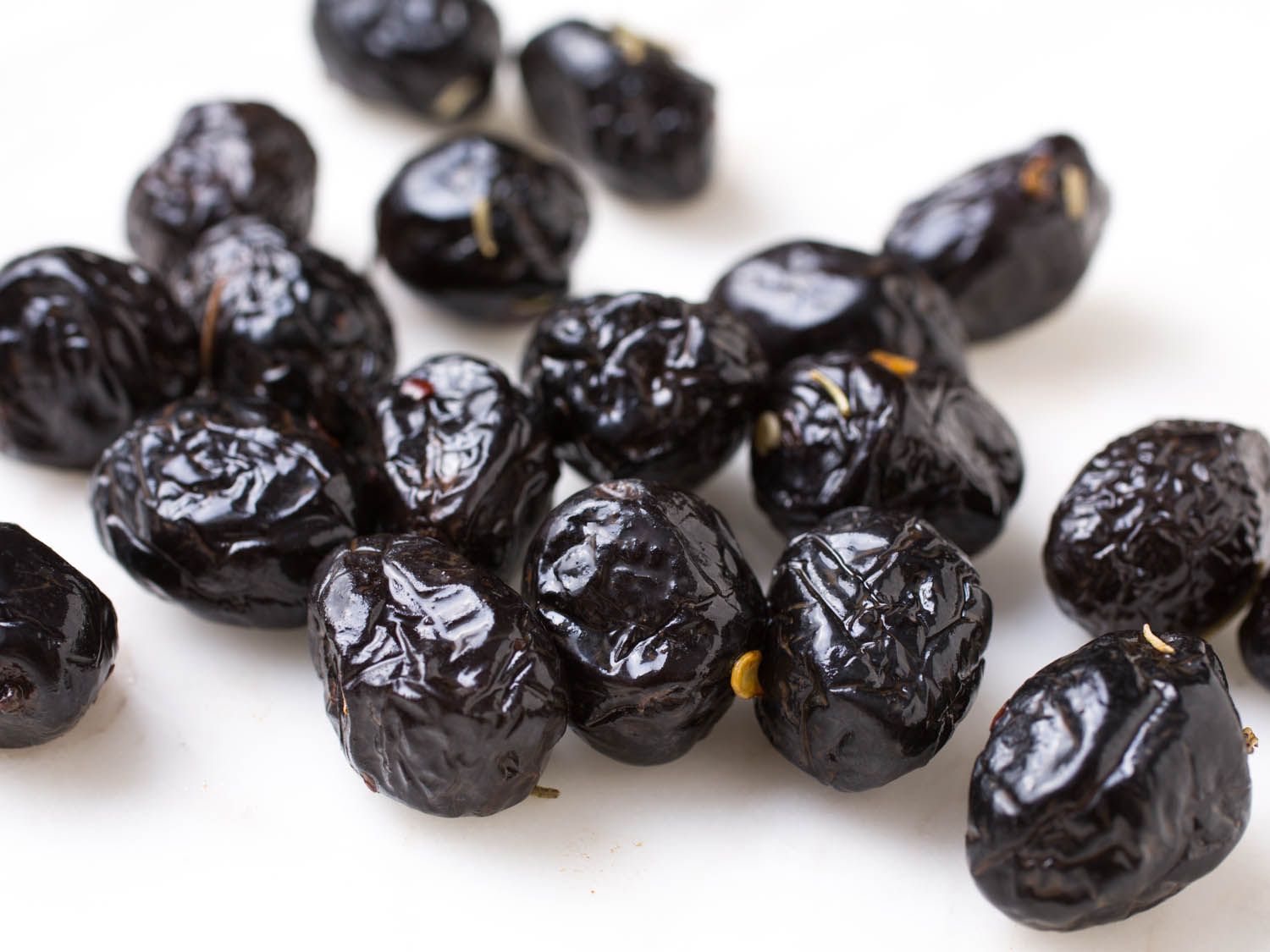 Closeup of shiny, very wrinkled black olives covered in chile flakes on white surface