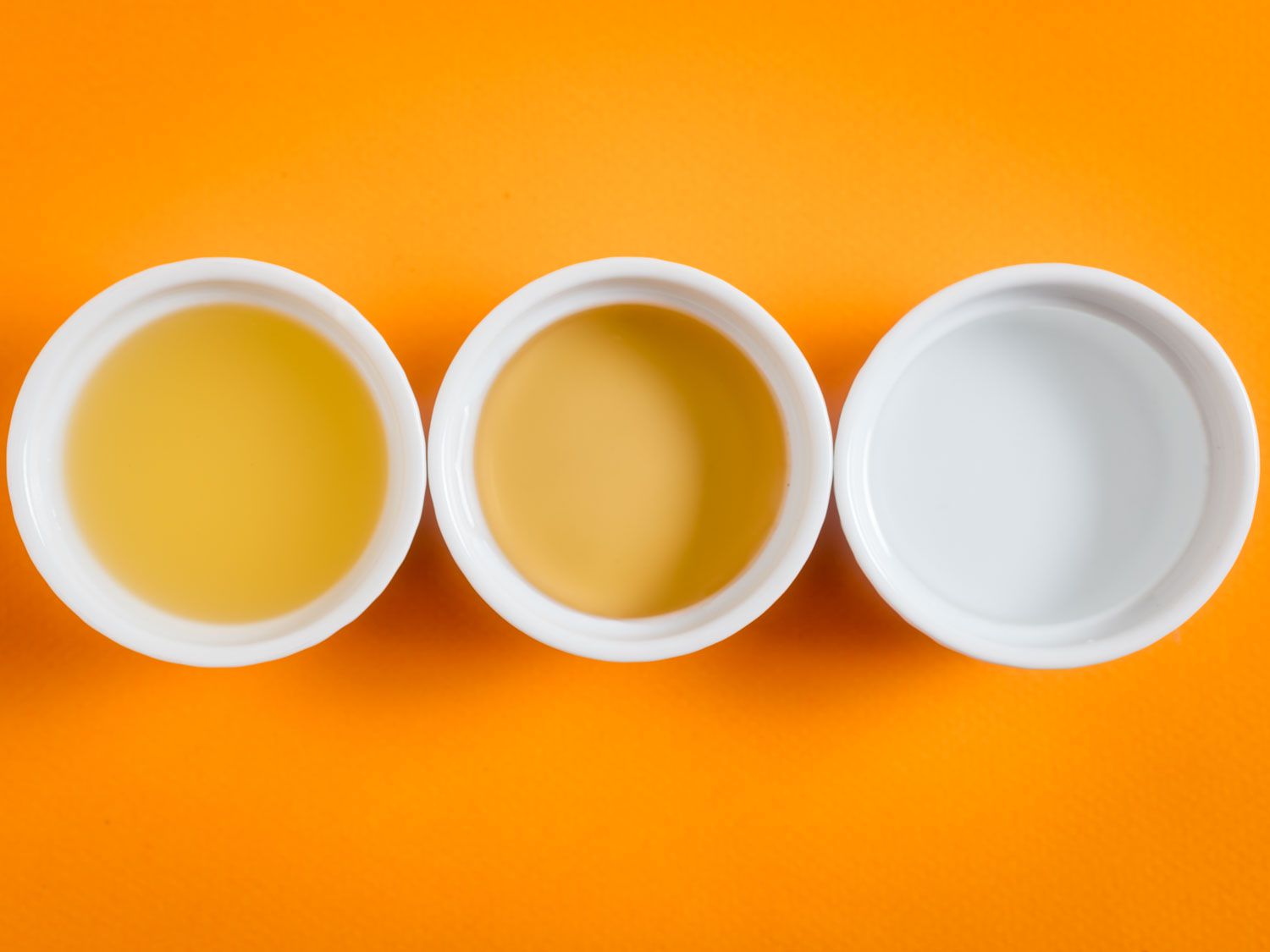 Overhead shot of three white ramekins of different vinegars, against an orange background