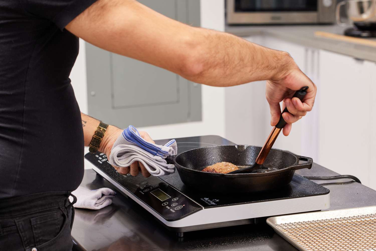 A cook sears a chicken breast in a pan set on a portable induction burner.