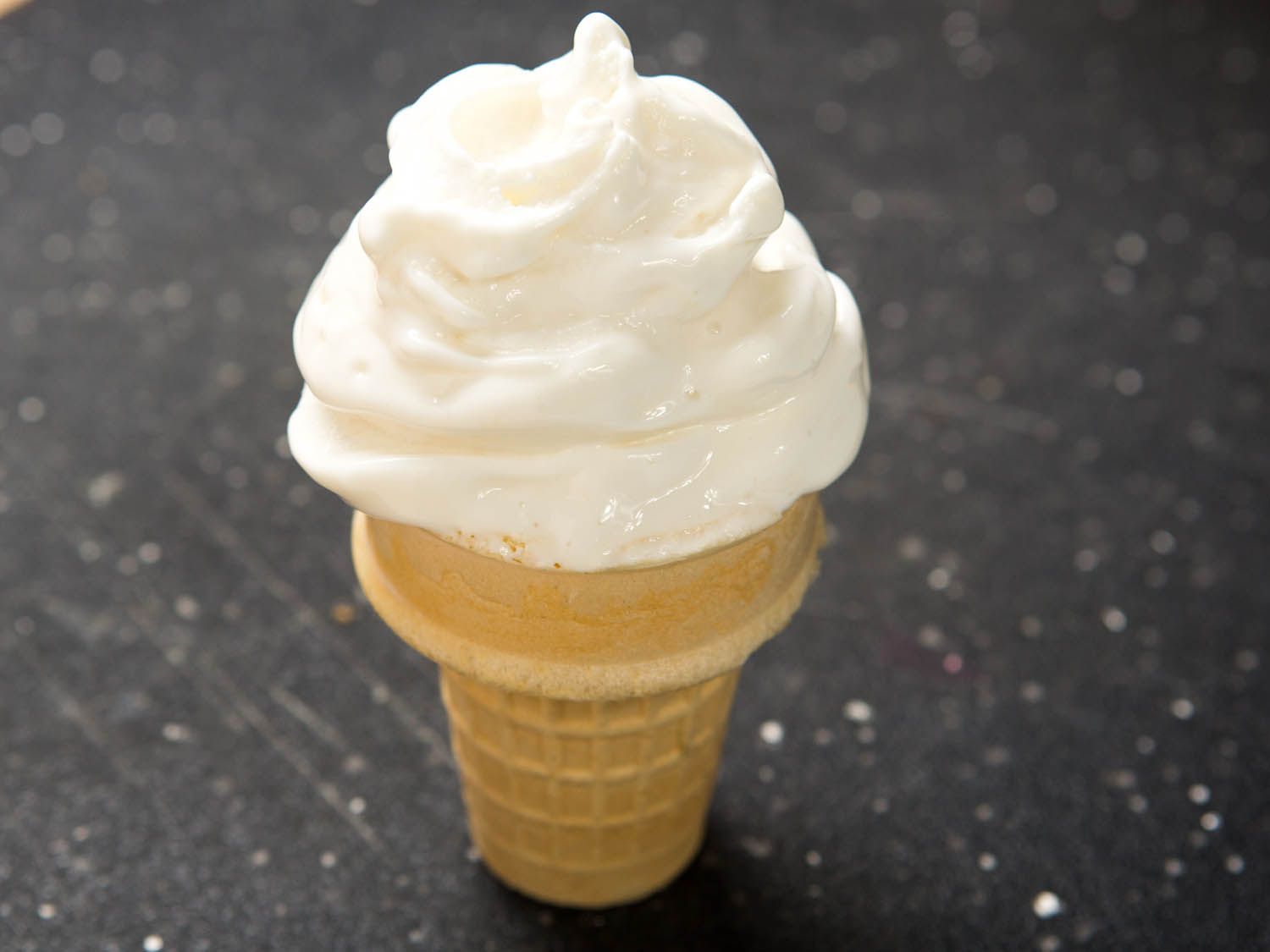 Swirls of soft-serve vanilla bean ice cream piled on a wafer ice cream cone.