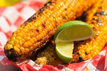 Corn with chile lime butter and lime wedges on a paper plate. 