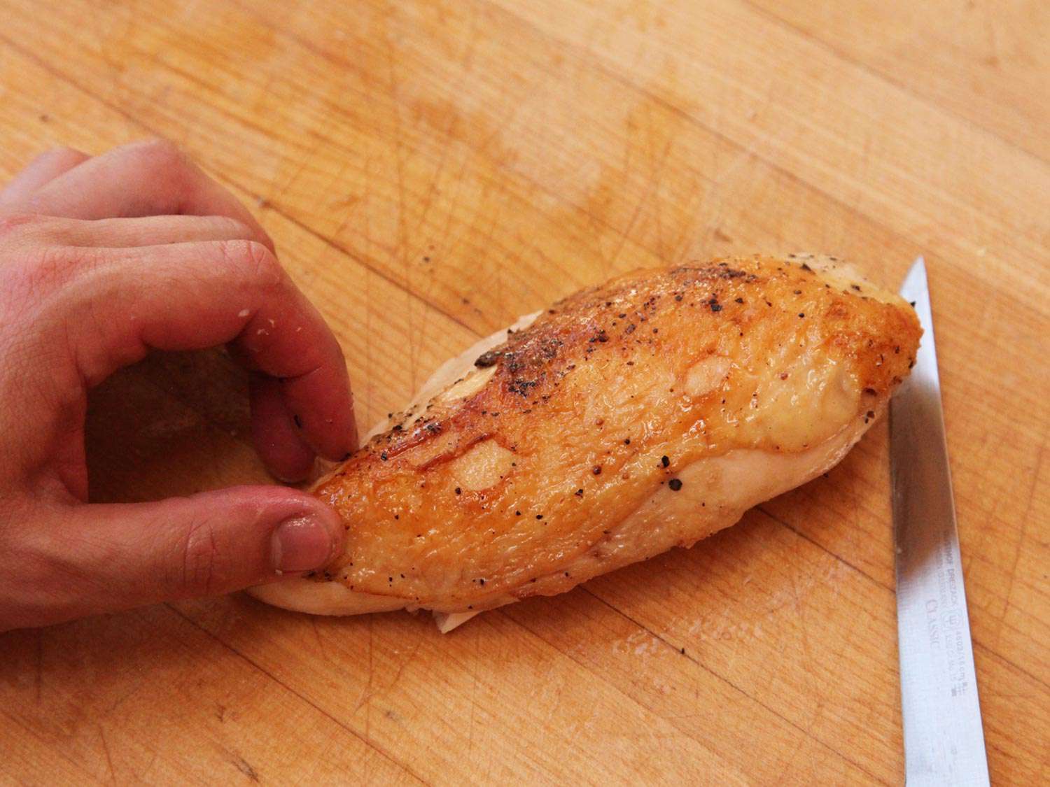 A chicken breast, cooked sous vide and finished on the stovetop with crispy, golden-brown skin. On a wooden cutting board next to a knife.