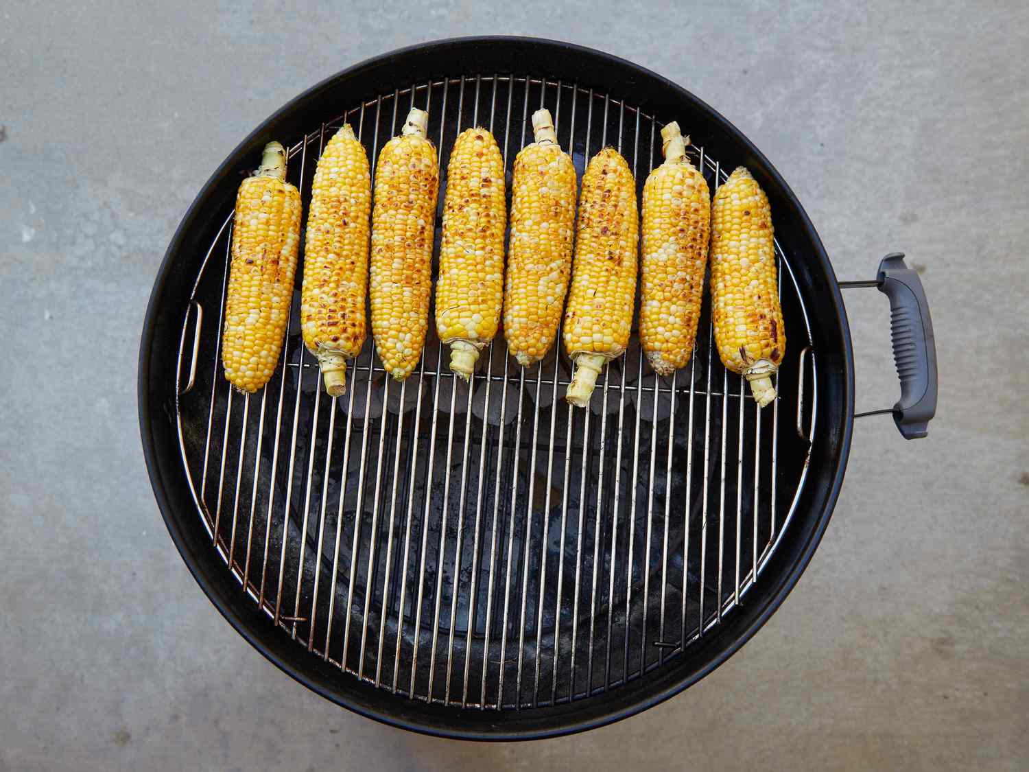Ears of corn being grilled on a round barbecue grill
