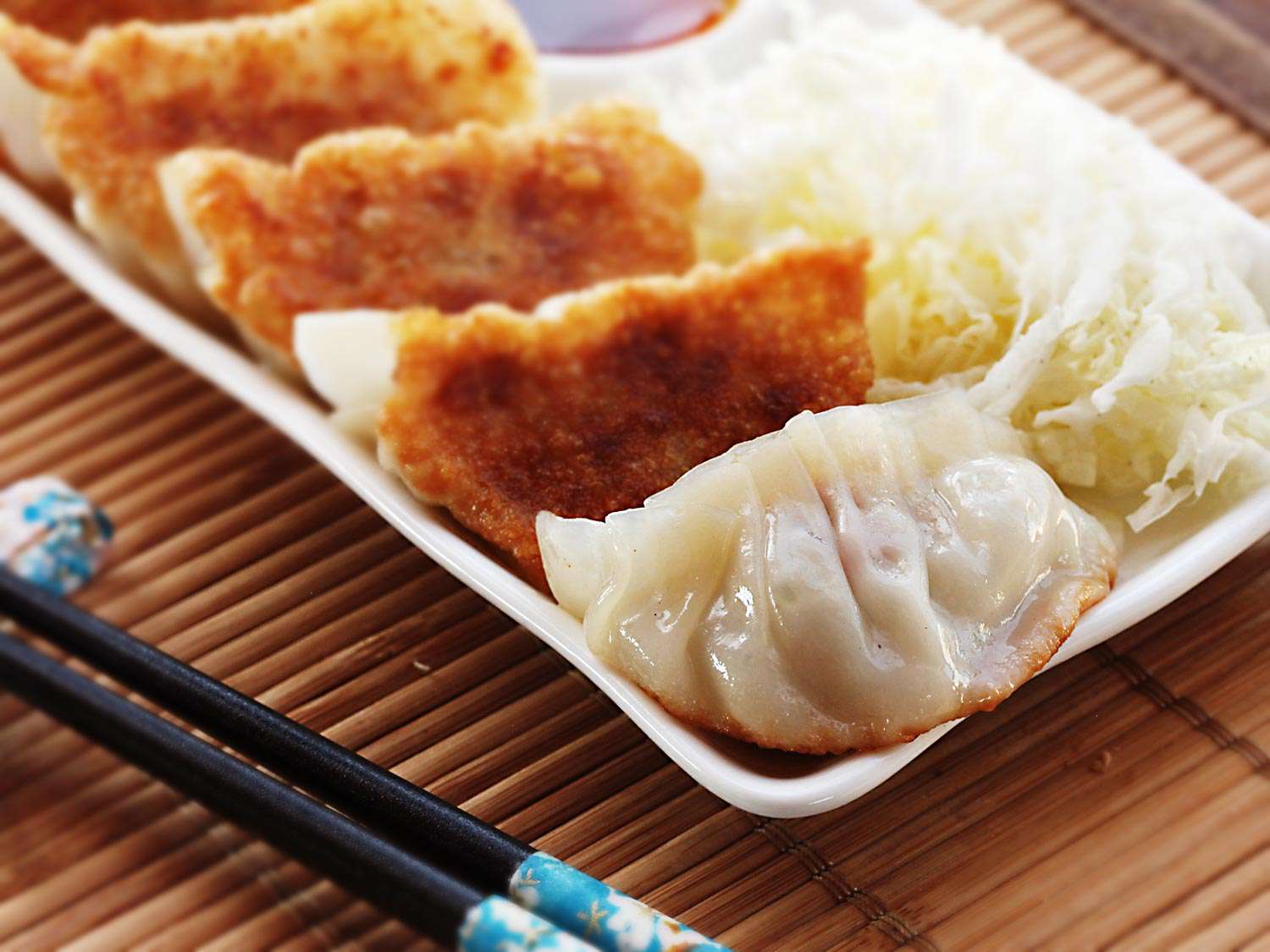 A platter of five pork and cabbage gyoza. Four of the dumplings are positioned crisp side facing up, and one dumpling is crisp-side down. A pair of chopsticks is next to the platter. 