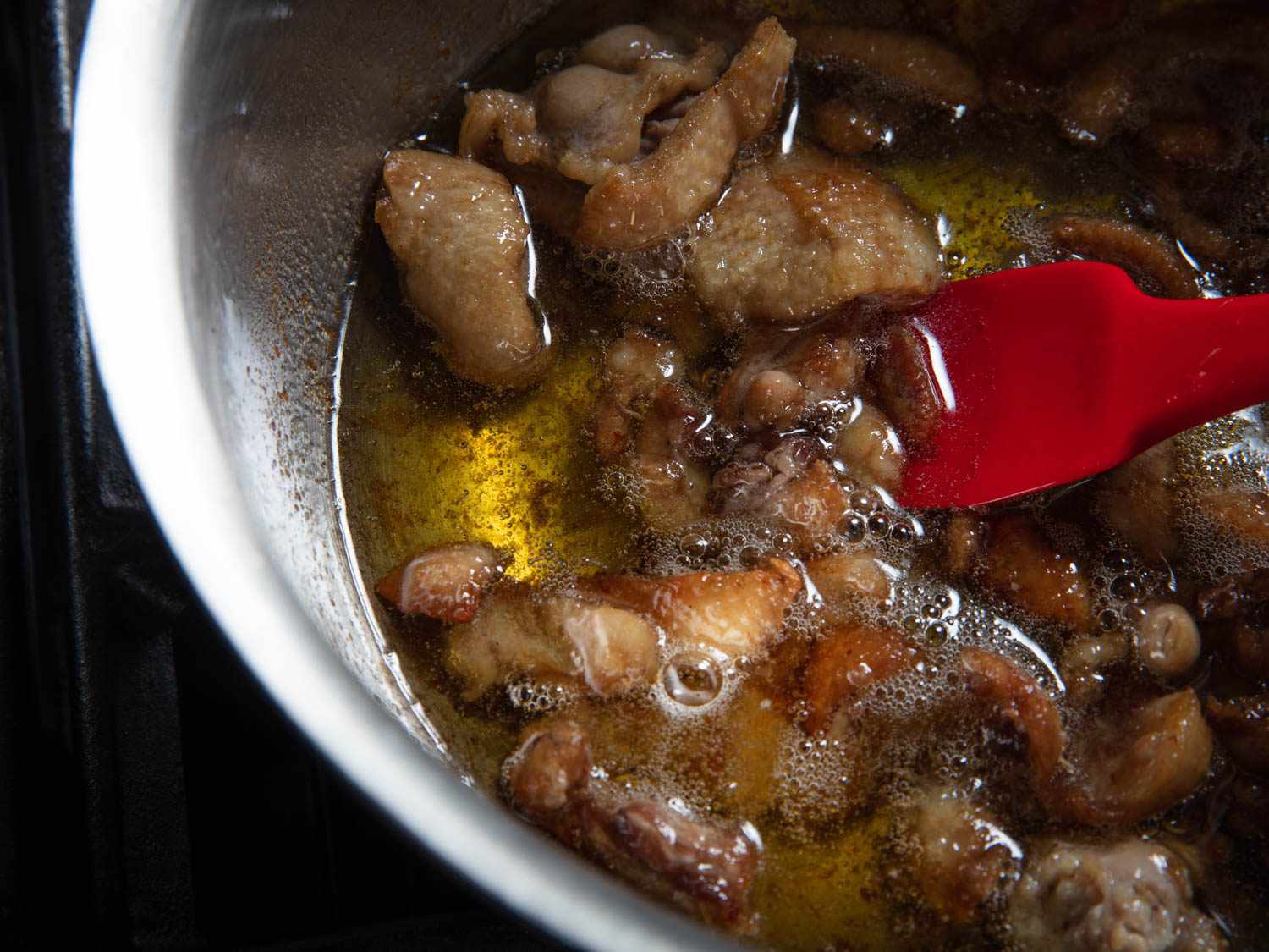 Closeup of stirring pieces of duck skin in clear golden duck fat.