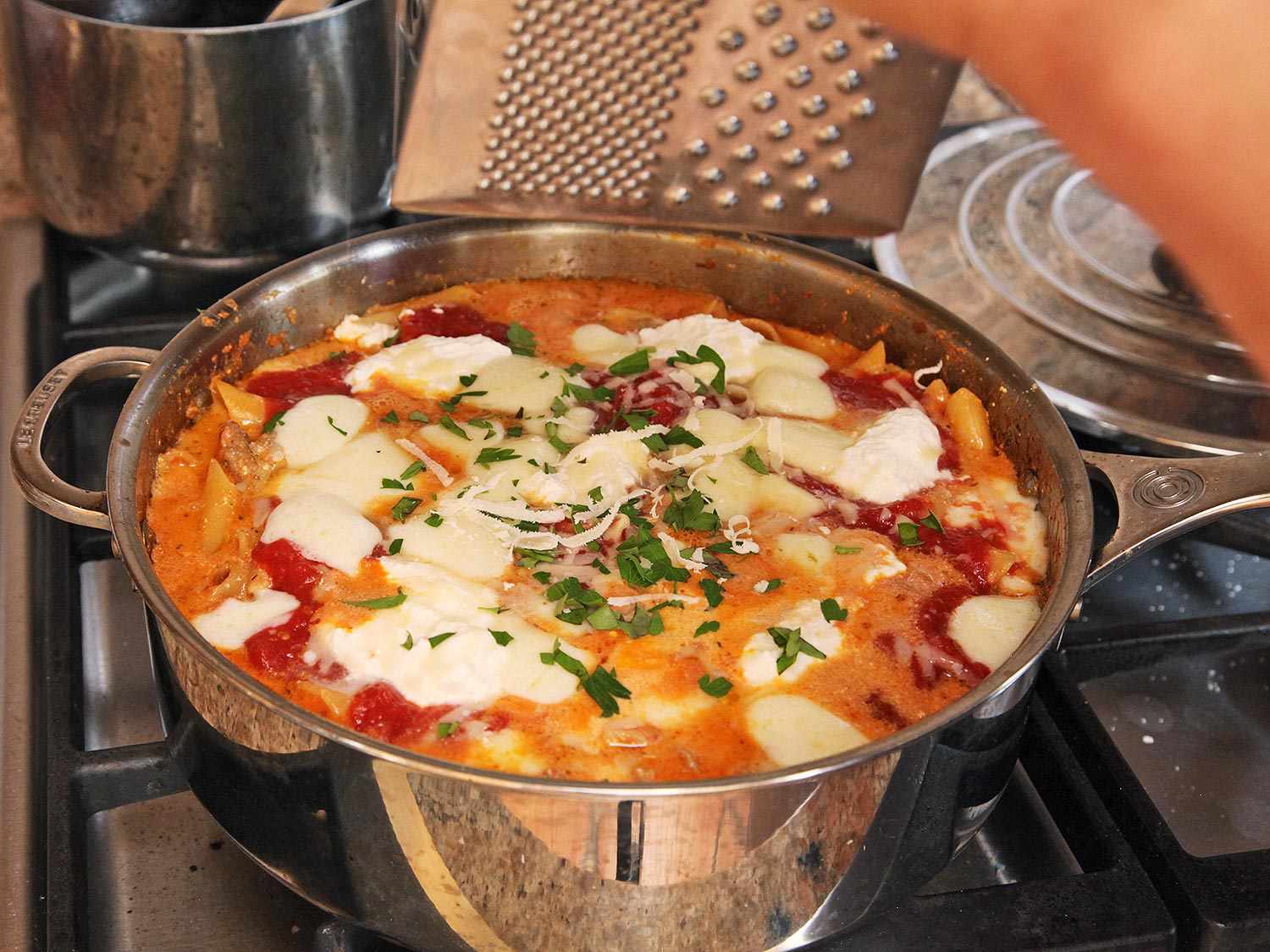 A saute pan full of ziti in tomato sauce and cheese.