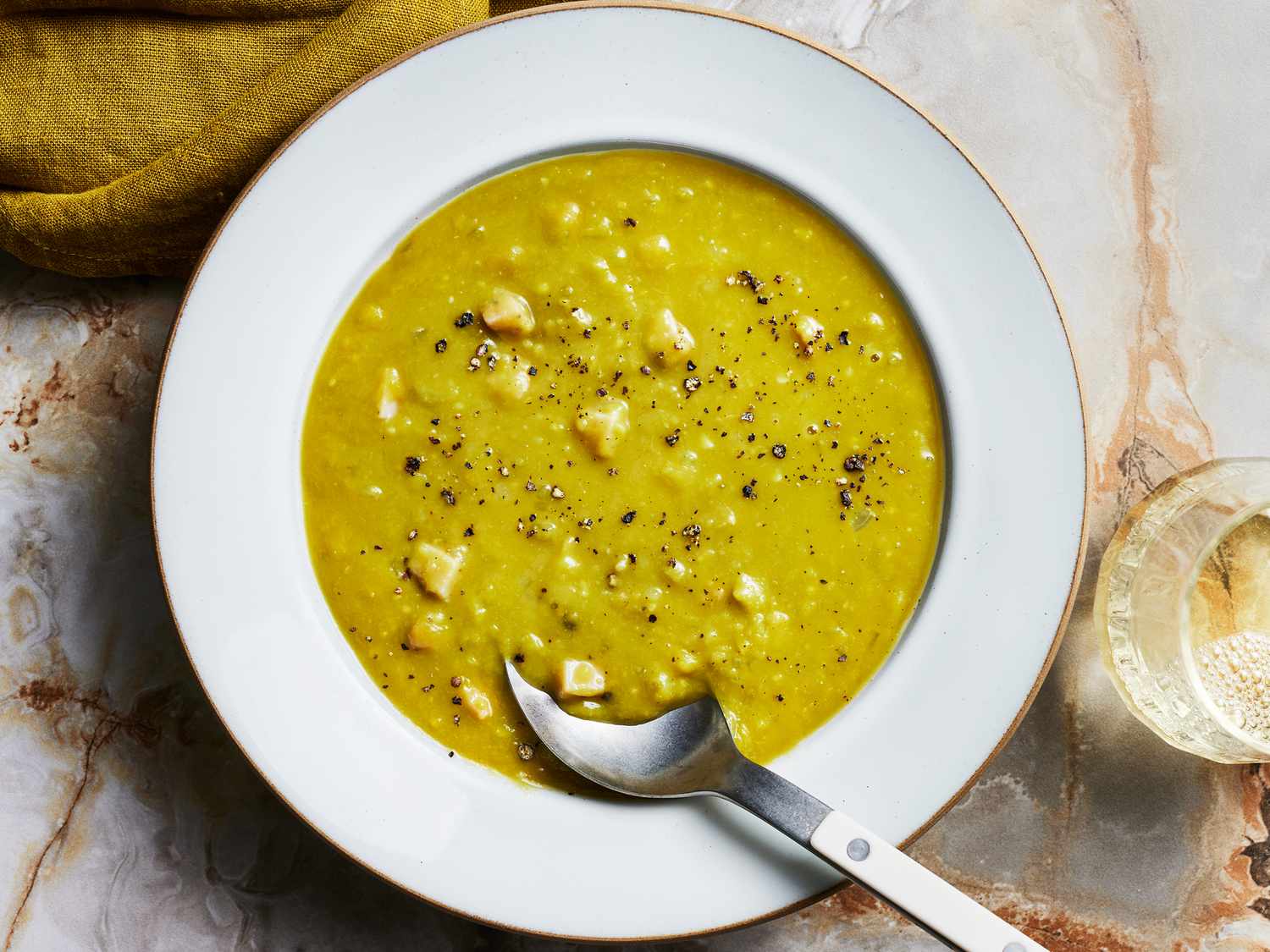 Split Pea Soup with a spoon, a green napkin and a drink, with a marble surface