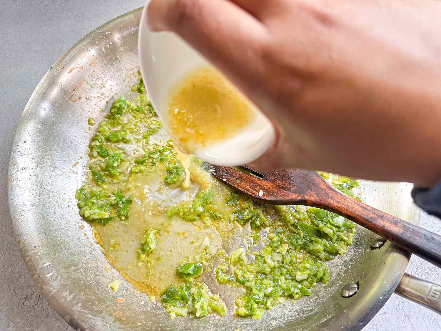 Sauce being added to a skillet with sautéd vegetables and a wooden spoon