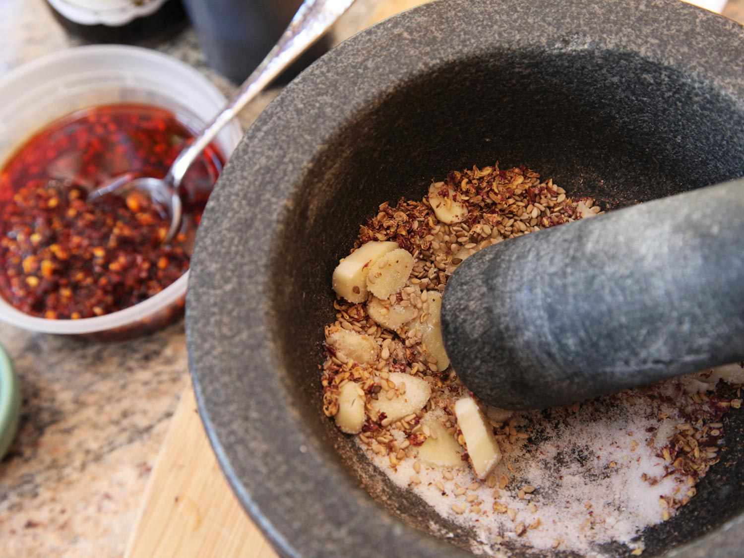 Grinding garlic cloves into dry chile mixture in mortar and pestle. 