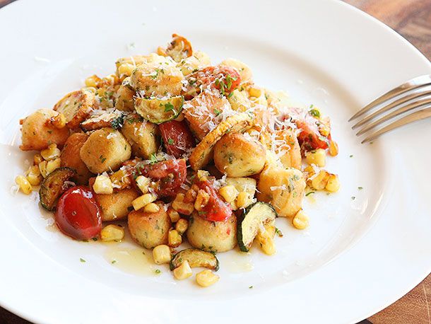 A large white plate of gnocchi with cherry tomatoes, corn, and zucchini, dusted with grated cheese and fresh herbs.