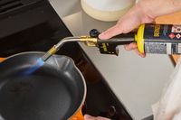 a person using the bernzomatic to heat a skillet