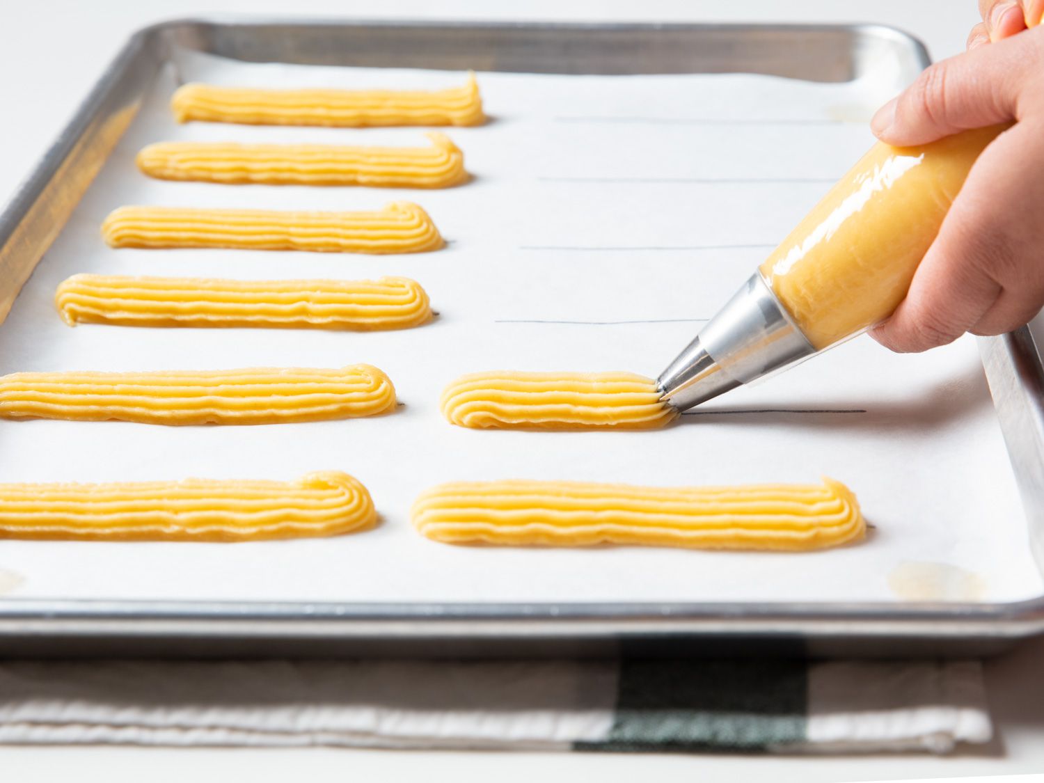 piping choux onto a baking sheet with parchment that's had lines drawn on it to guide the size of each éclair