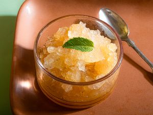 A glass bowl of granita topped with a single mint leaf, placed next to a spoon