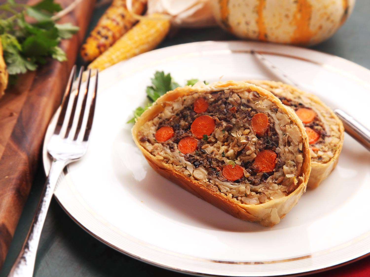 Two slices of vegetables Wellington resting on a place with cutlery alongside.