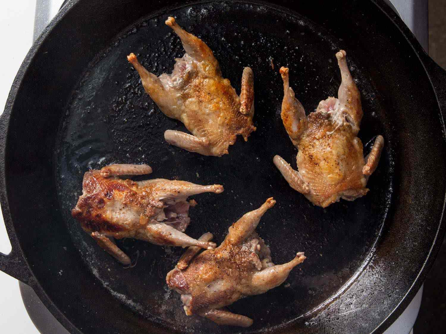 Four whole quails cooking in a cast iron skillet
