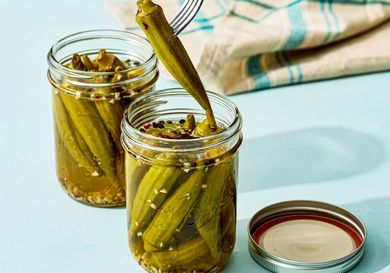 Two jars of pickled okra one jar with a fork lifting a piece of okra