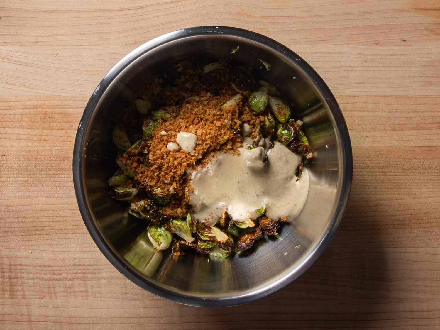 The shaved and roasted Brussels sprouts in a mixing bowl with the breadcrumbs and dressing before mixing.