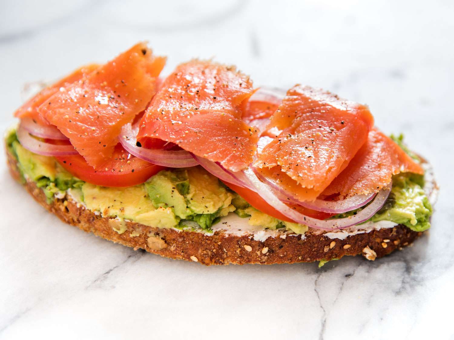A composed avocado toast with smoked salmon on a marble surface.