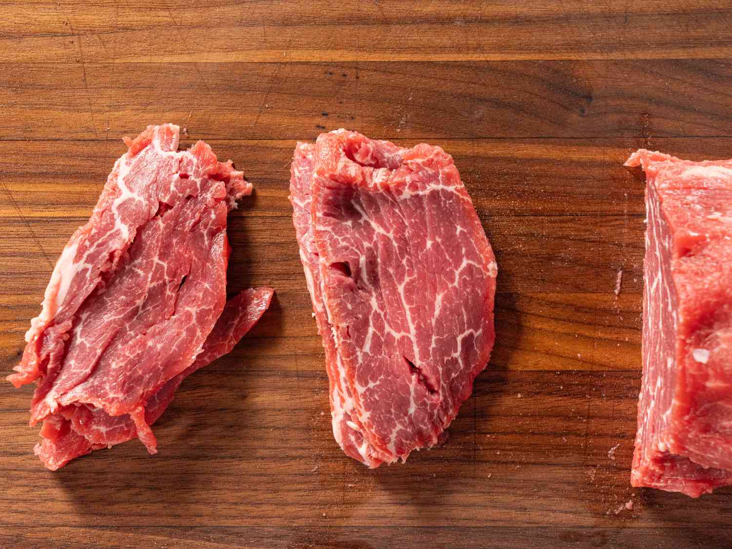Large piece of beef with a few thin slices on a wooden board