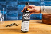 A person holding a bottle labeled "Black Sesame Oil" in a kitchen setting