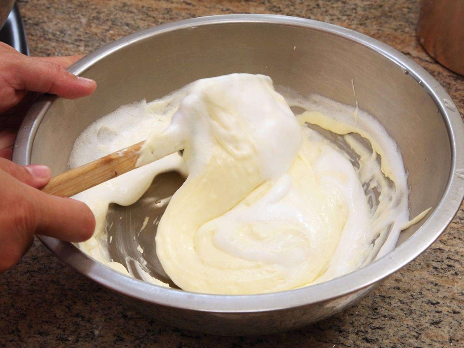 Whipped egg whites are folded into the cheesecake batter with a spatula.