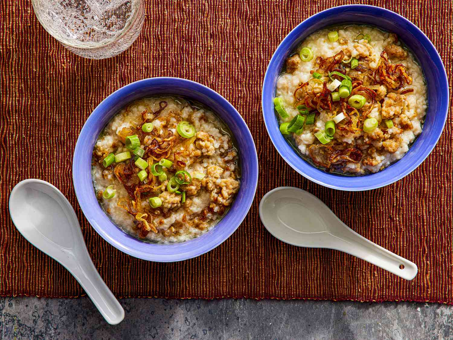 Overhead view of two bowls of congee on a brown woven placemat