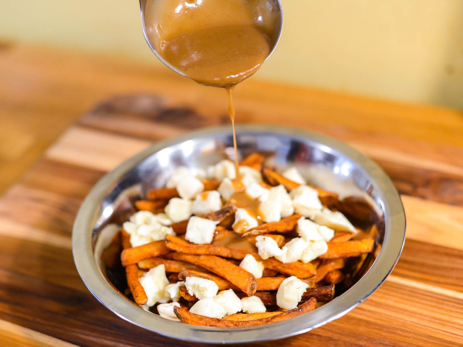 Ladling hot gravy onto a plate of fries and cheese curds. 