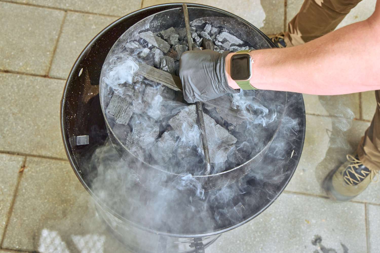 A person places charcoal into the Pit Barrel Cooker Co. Classic Pit Barrel Cooker