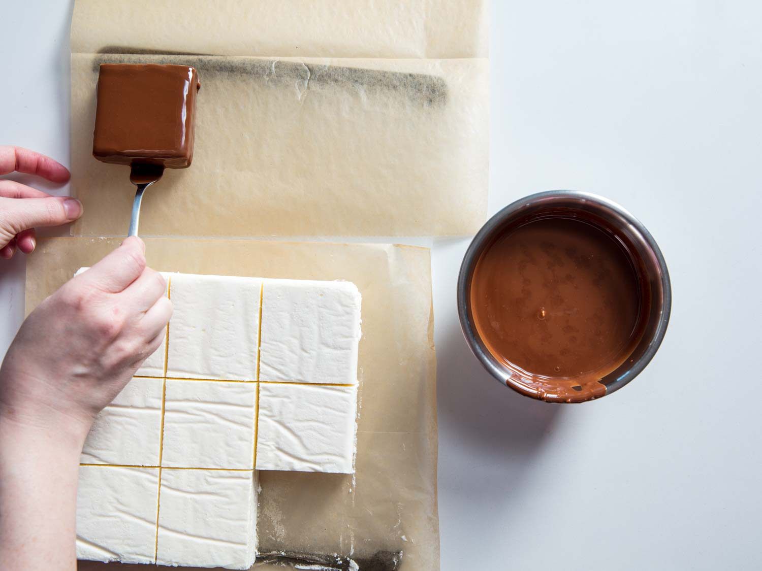 Placing a chocolate-dipped ice cream square on parchment for homemade Klondike Bars.