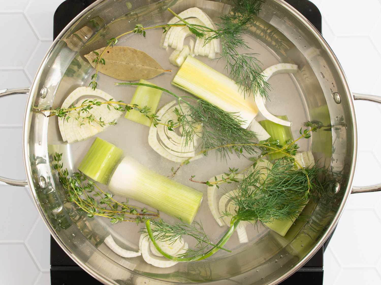 1 quart of cold water, lemon juice, leek or onion, celery, fennel, thyme and dill, bay leaf, and a large pinch of salt combined inside a large saucepan.