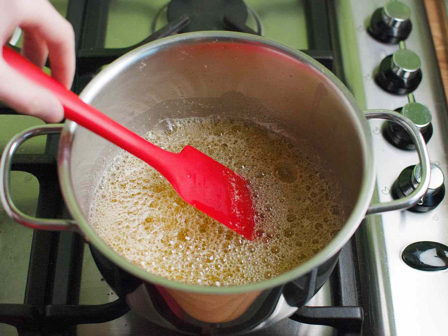 A silicone spatula stirring a pot of melted butter. The surface of the butter is covered in small bubbles.