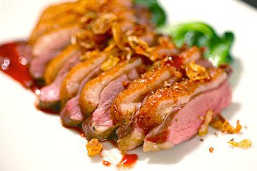 Sliced seared sous vide duck breast on a white plate with sauce and sautéed greens.