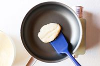 Using a blue silicone food turner to flip a pancake in a skillet