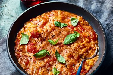 Bowl of Pappa Al Pomodoro in a black bowl on dark blue surface, with dark dyed napkin and a glass of red wine 