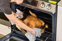 A person removing the KellyBronze Turkey from the oven