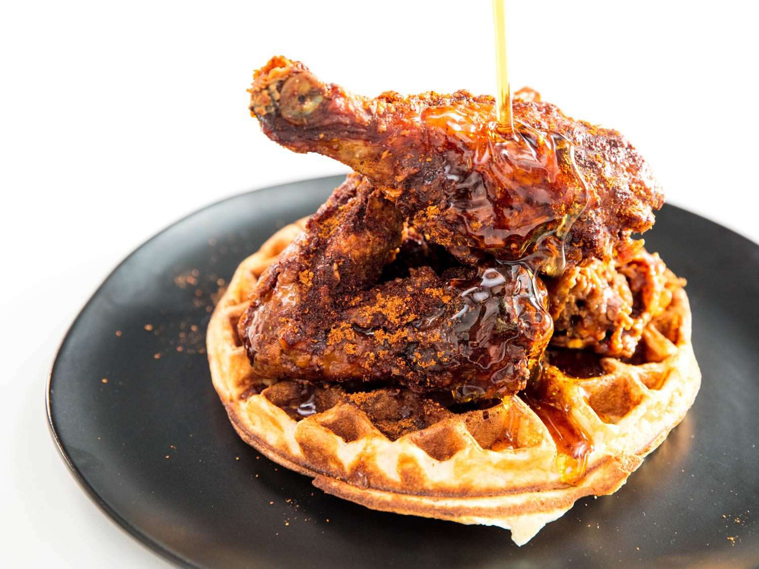 A honey- and chili-dusted piece of fried chicken topping a waffle on a plate