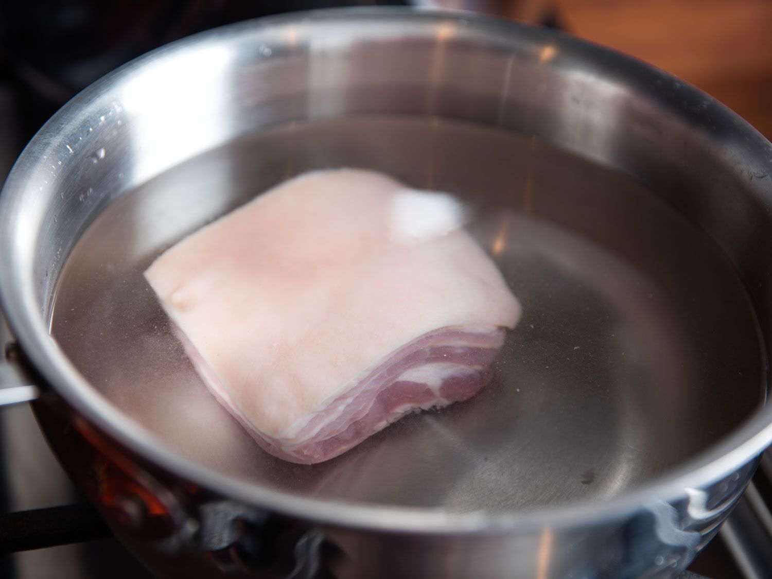 A small slab of salt pork submerged in a saucepan half-full of water, ready to be simmered for choucroute garnie.