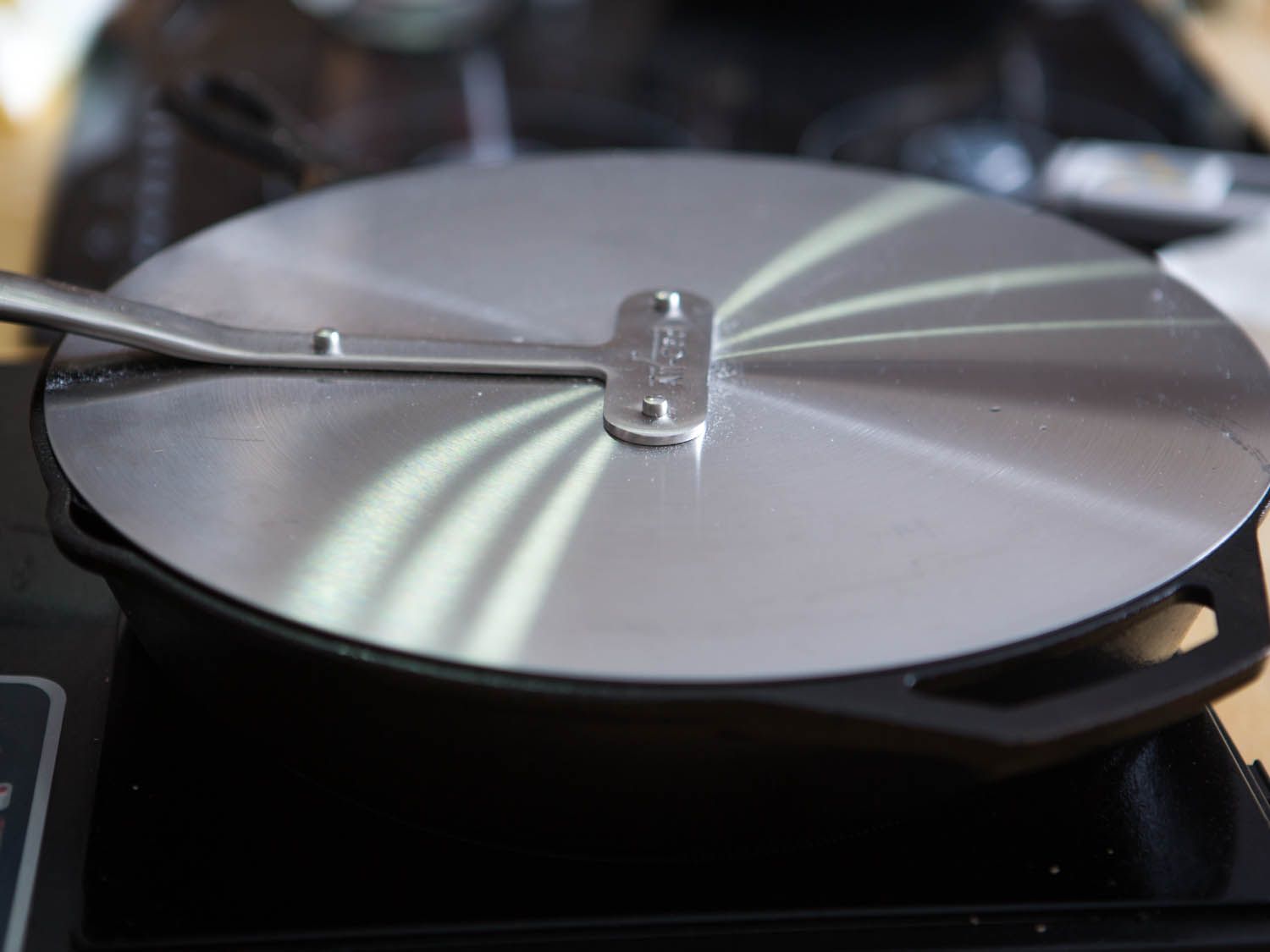A lid over a cast iron pan filled with pieces of frying chicken.