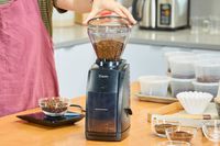 A person uses the Baratza Encore Conical Burr Coffee Grinder to grind coffee beans
